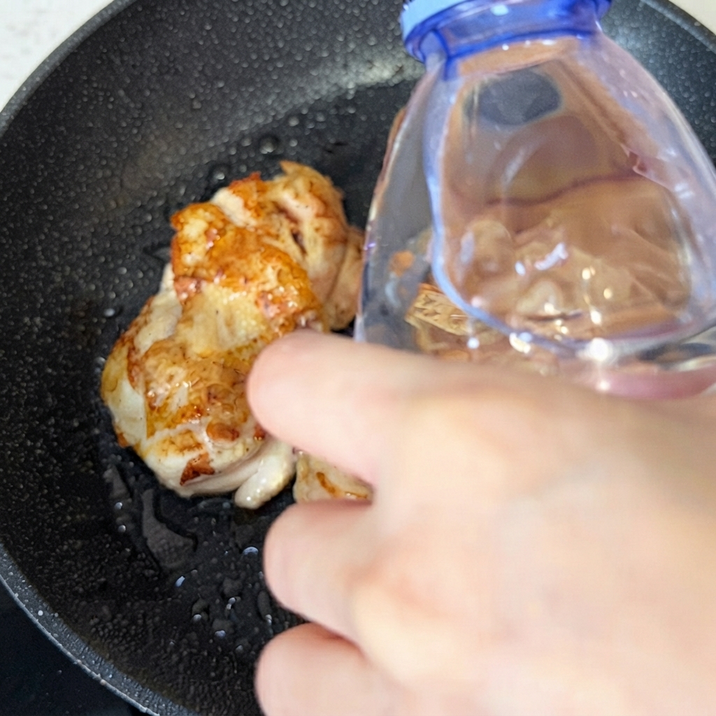 Un petit filet deau versé dans la poêle contenant les morceaux de poulet dorés.
