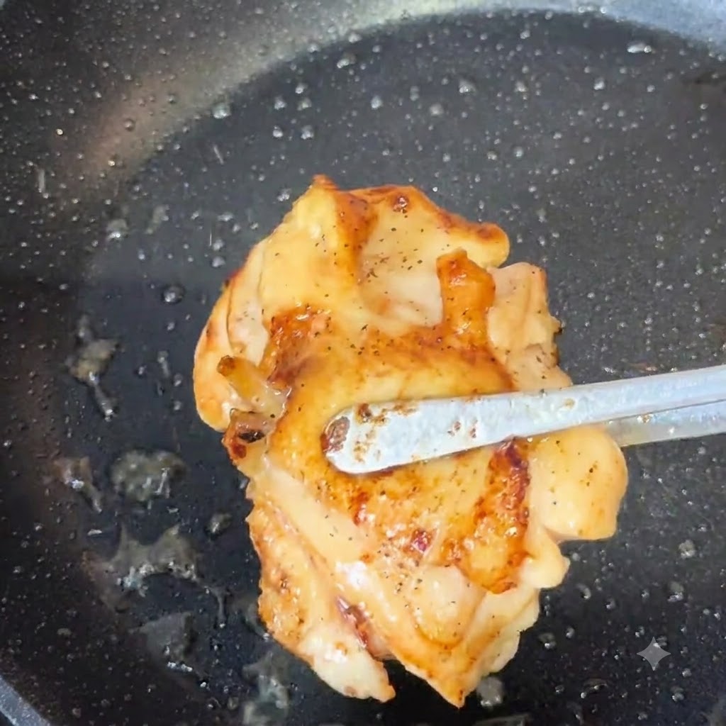 Une pince de cuisine soulevant un haut de cuisse de poulet bien doré dune poêle.