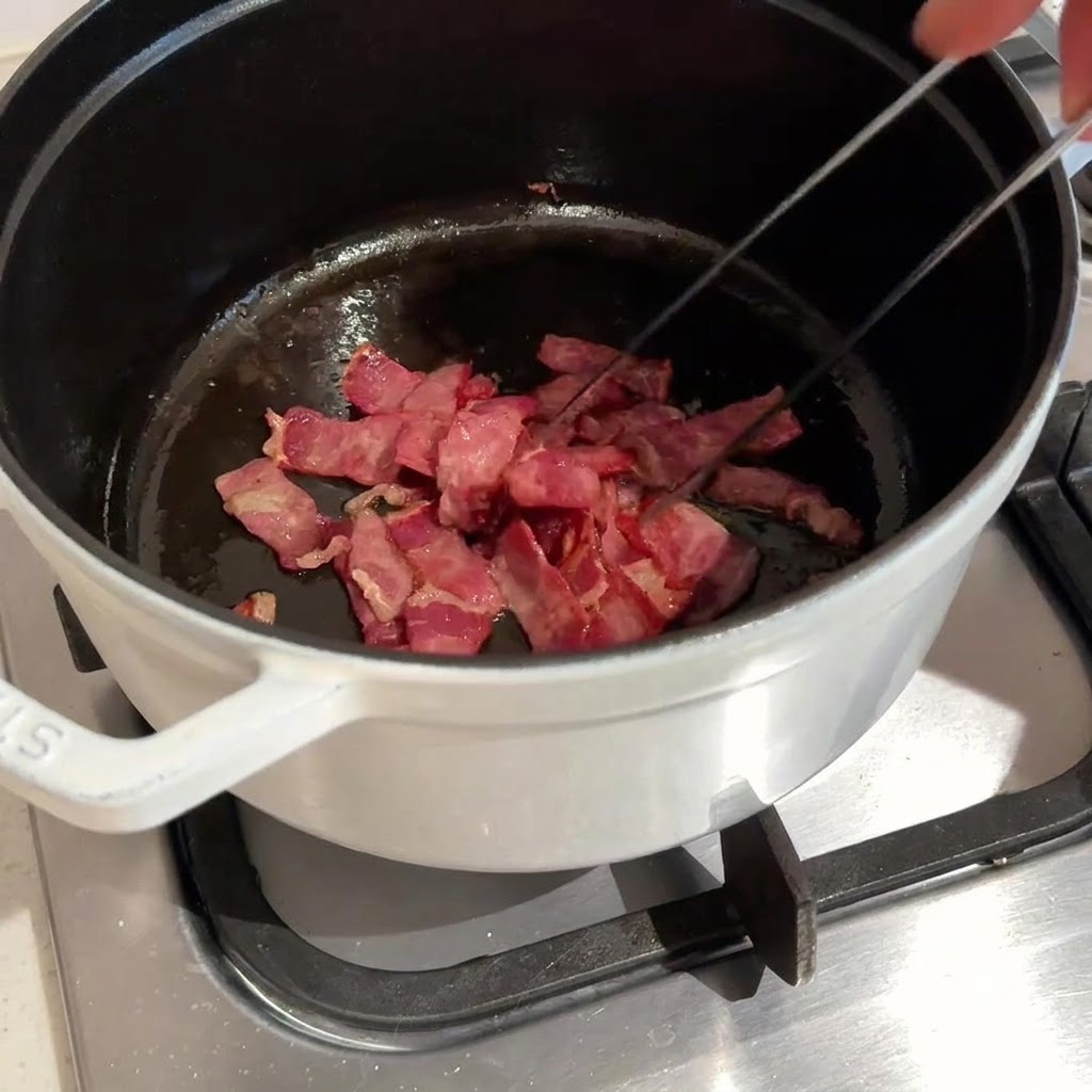 Du bacon haché en train dêtre mélangé et frit dans une casserole sombre à laide de pinces en métal.