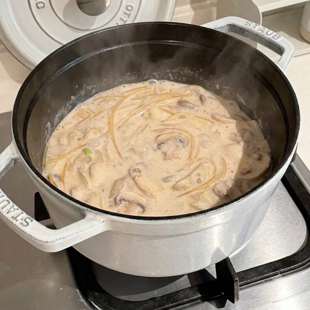Des spaghettis cuisant dans un bouillon crémeux frémissant à lintérieur dune casserole blanche.