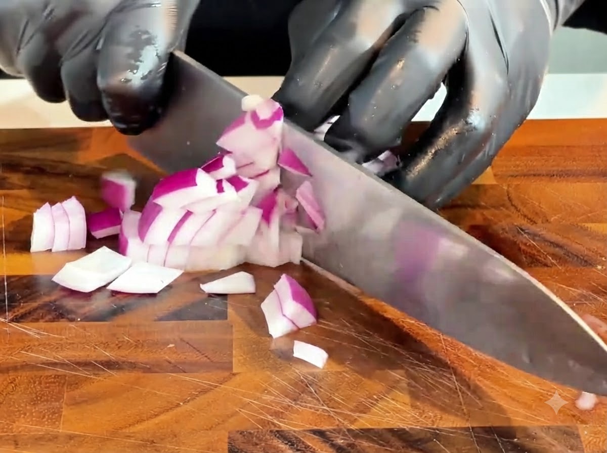 Un couteau coupant un oignon rouge cru en petits morceaux sur une planche à découper en bois.