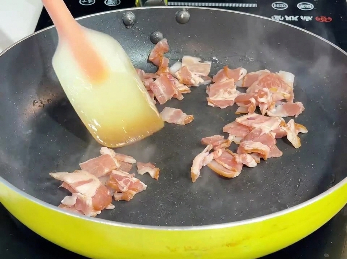 Du bacon et de loignon sautés avec une spatule dans une poêle.