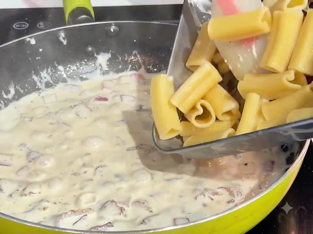 Des pâtes en forme de cœur précuites versées dun plateau dans une sauce crémeuse au bacon bouillonnante dans une poêle.