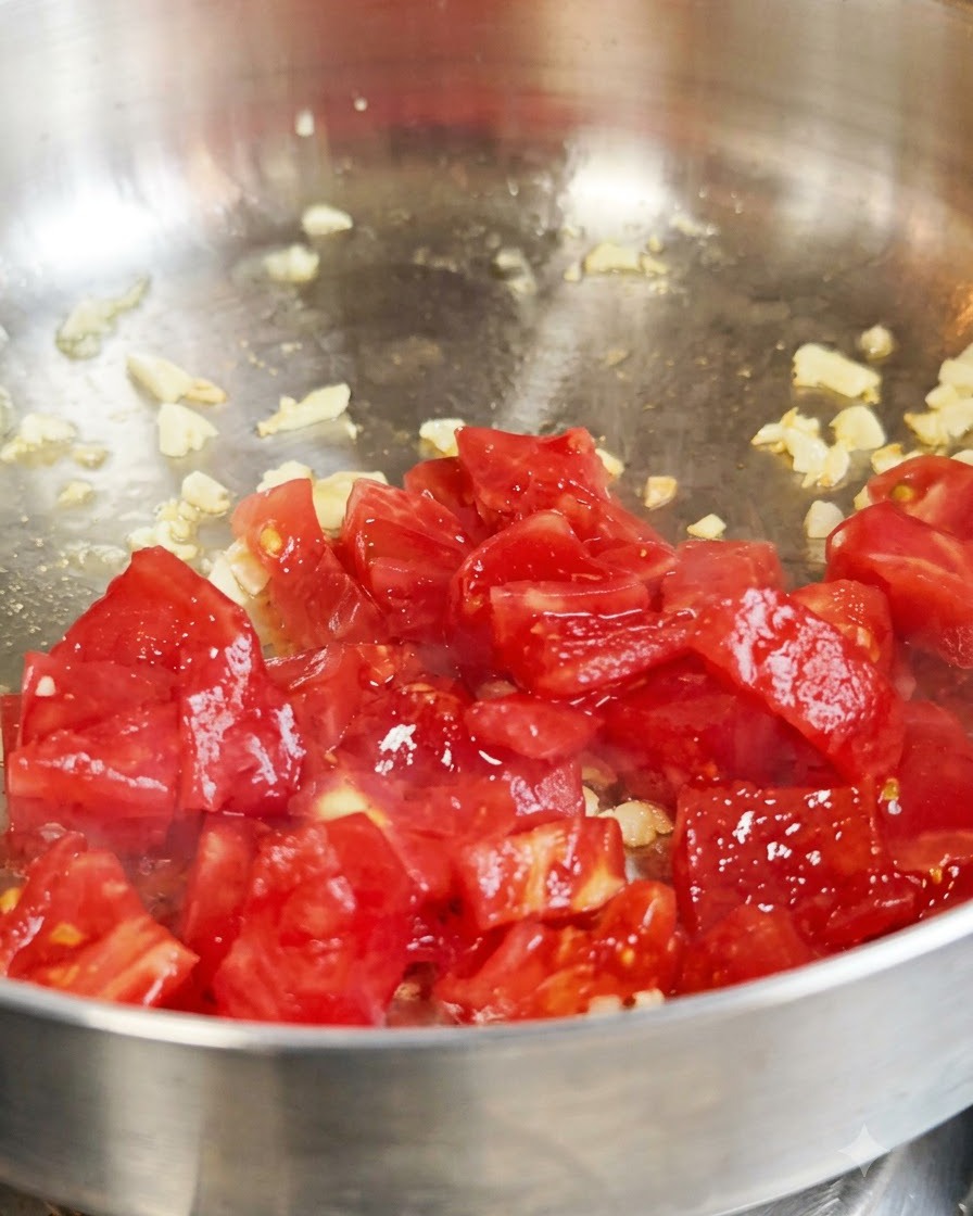 Tomates rouges fraîches coupées en dés en train dêtre sautées avec de lail à lintérieur dune poêle en métal.