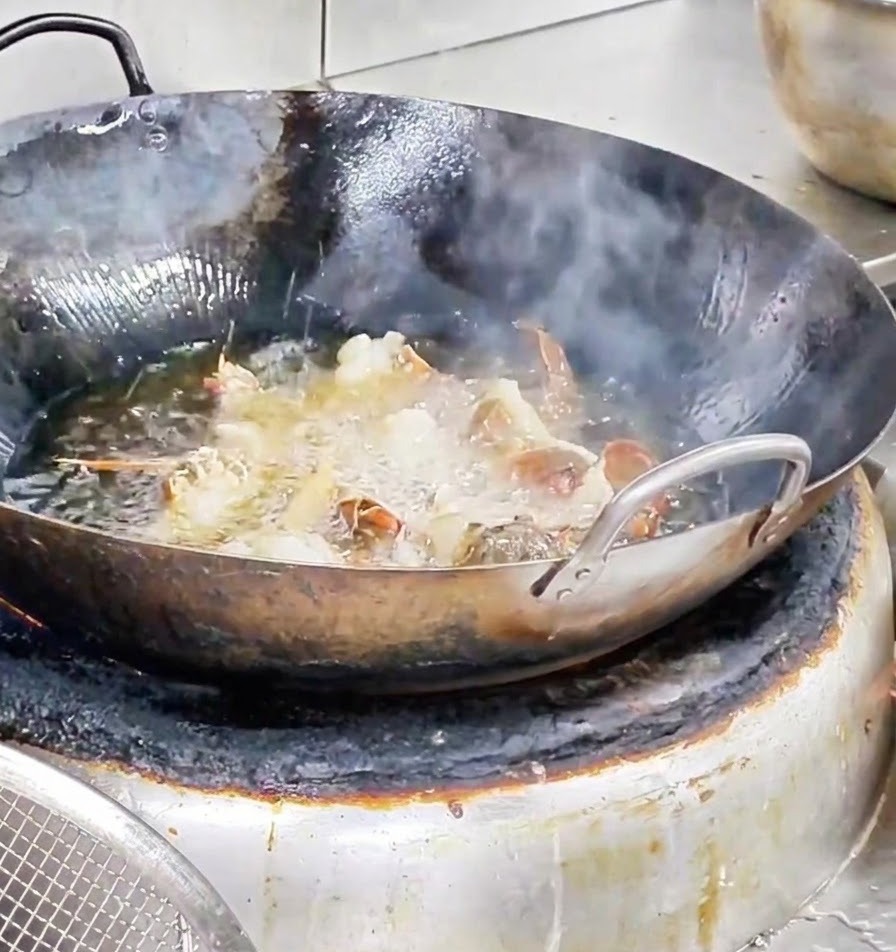Morceaux de homard frits vigoureusement dans un wok rempli dhuile chaude bouillante.