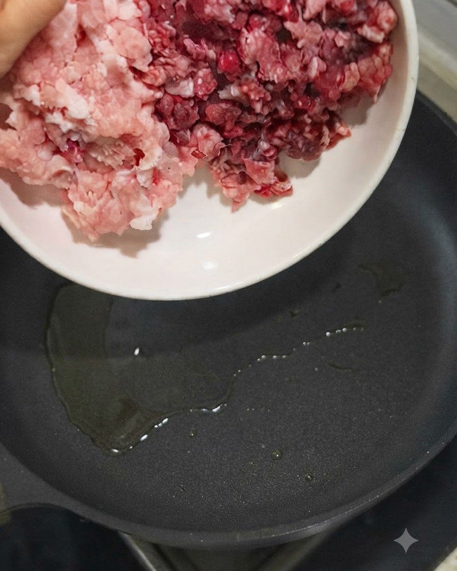 Du porc haché et du bœuf haché versés dun bol blanc dans une poêle huilée bien chaude.