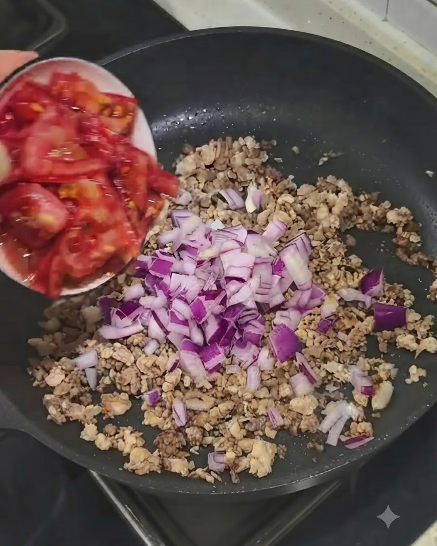 Des tomates fraîches coupées ajoutées depuis un petit bol dans la poêle avec la viande et les oignons.