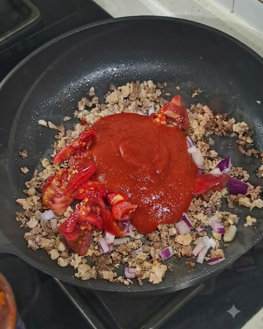Une cuillerée de concentré de tomate posée sur le mélange de viande et de légumes dans la poêle.