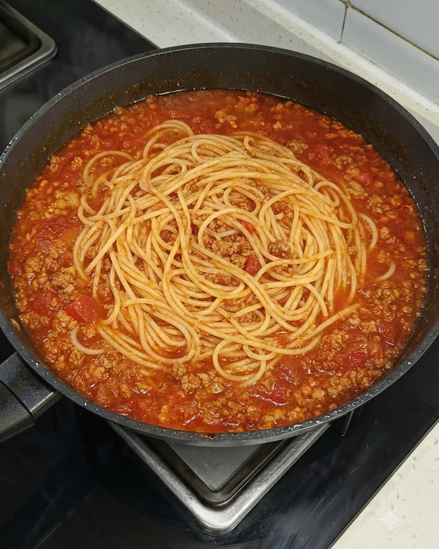 Un nid de spaghettis reposant uniformément au centre dune grande poêle remplie de sauce tomate à la viande sur une cuisinière.