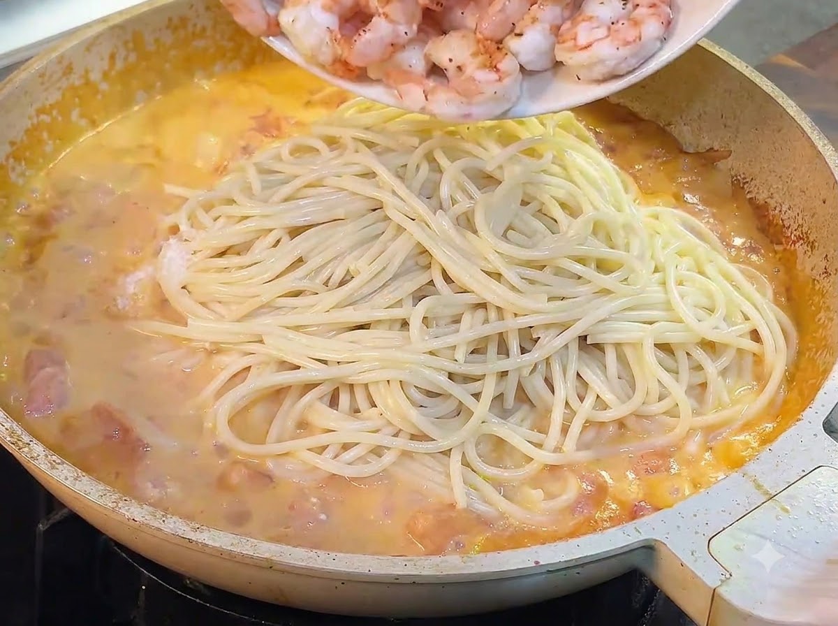 Des crevettes cuites versées dune assiette dans la poêle avec les spaghettis et la sauce.