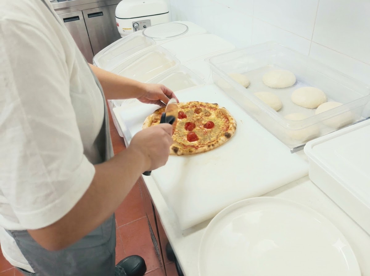 Personne utilisant une roulette à pizza pour couper une pizza fraîchement cuite sur une planche blanche.