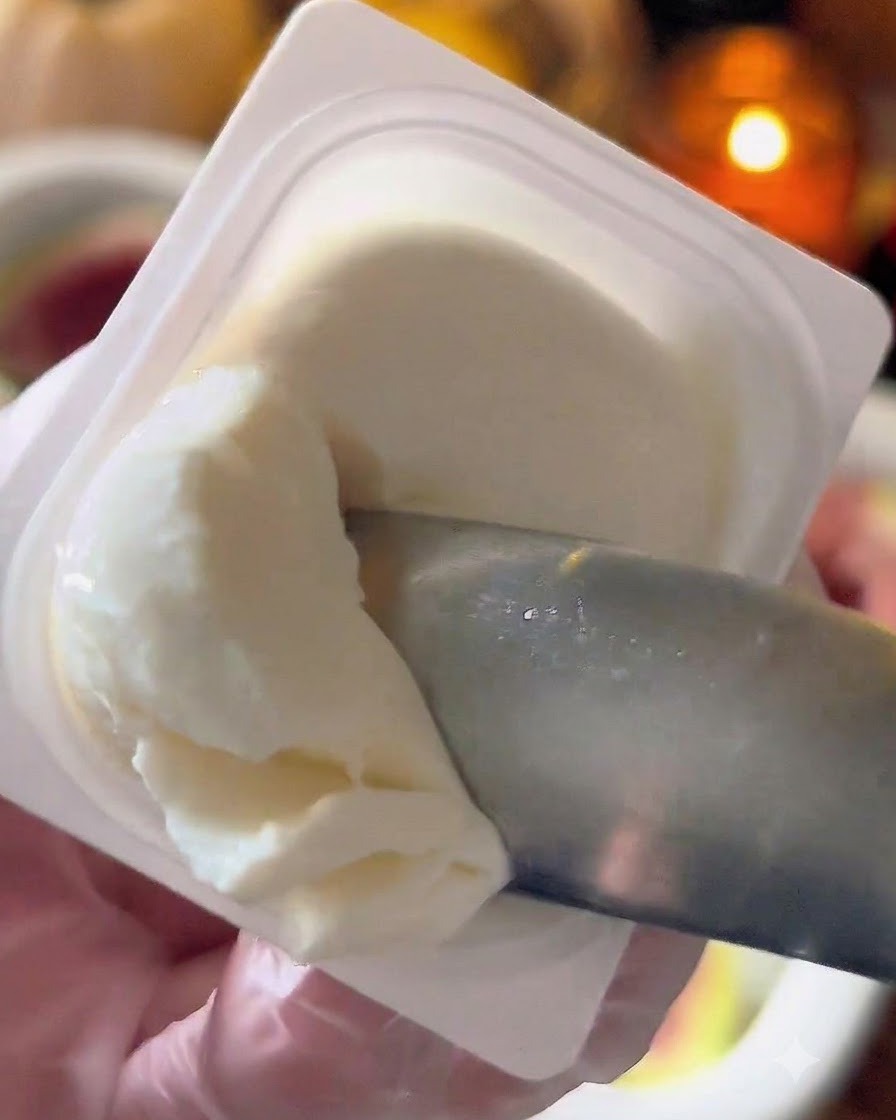 Un petit couteau ou une cuillère prélevant du fromage labneh blanc dans un récipient.