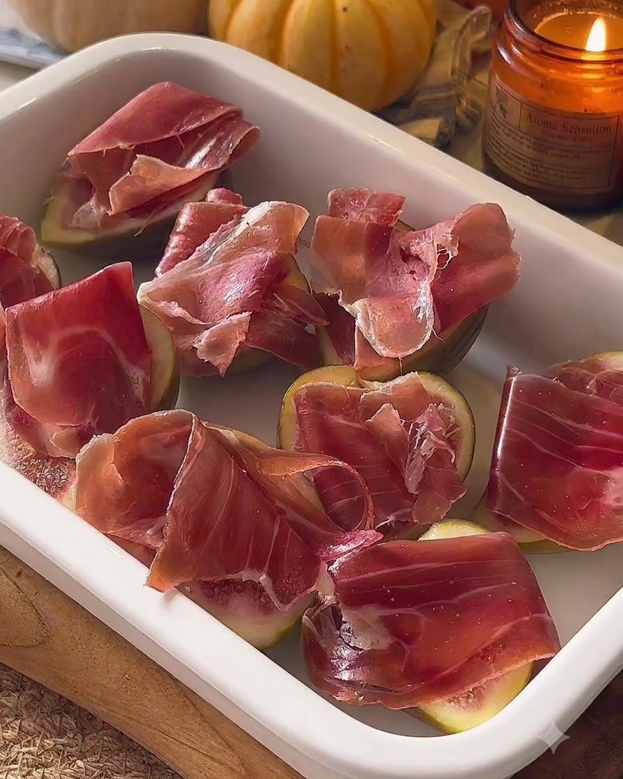 Figues assemblées et surmontées de prosciutto disposées dans un plat de cuisson blanc.