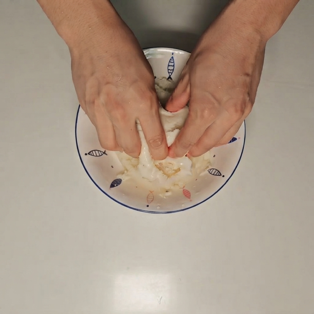 Des mains écrasant un petit pain vapeur mouillé à lintérieur dun bol blanc.