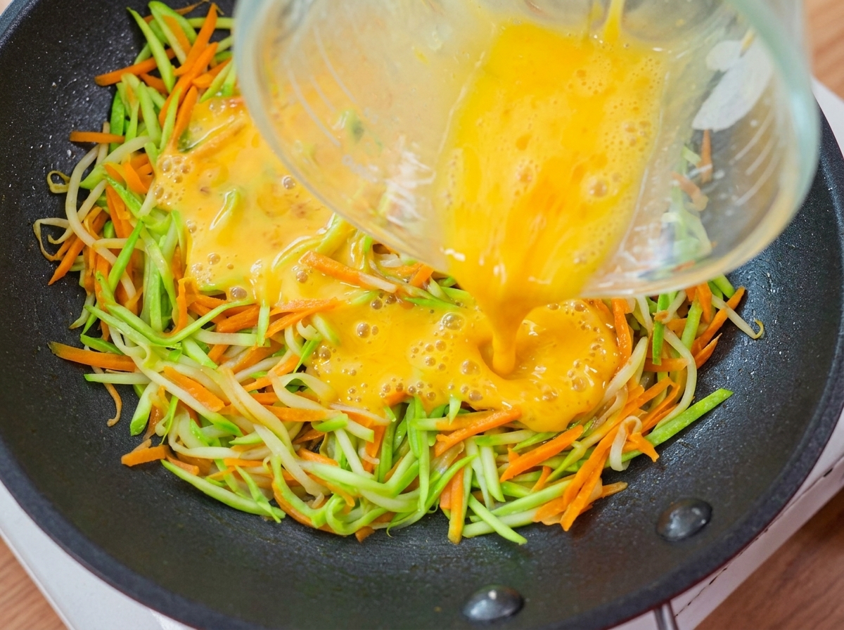 Du liquide dœuf jaune versé à partir dun verre mesureur sur la couche de légumes dans la poêle.
