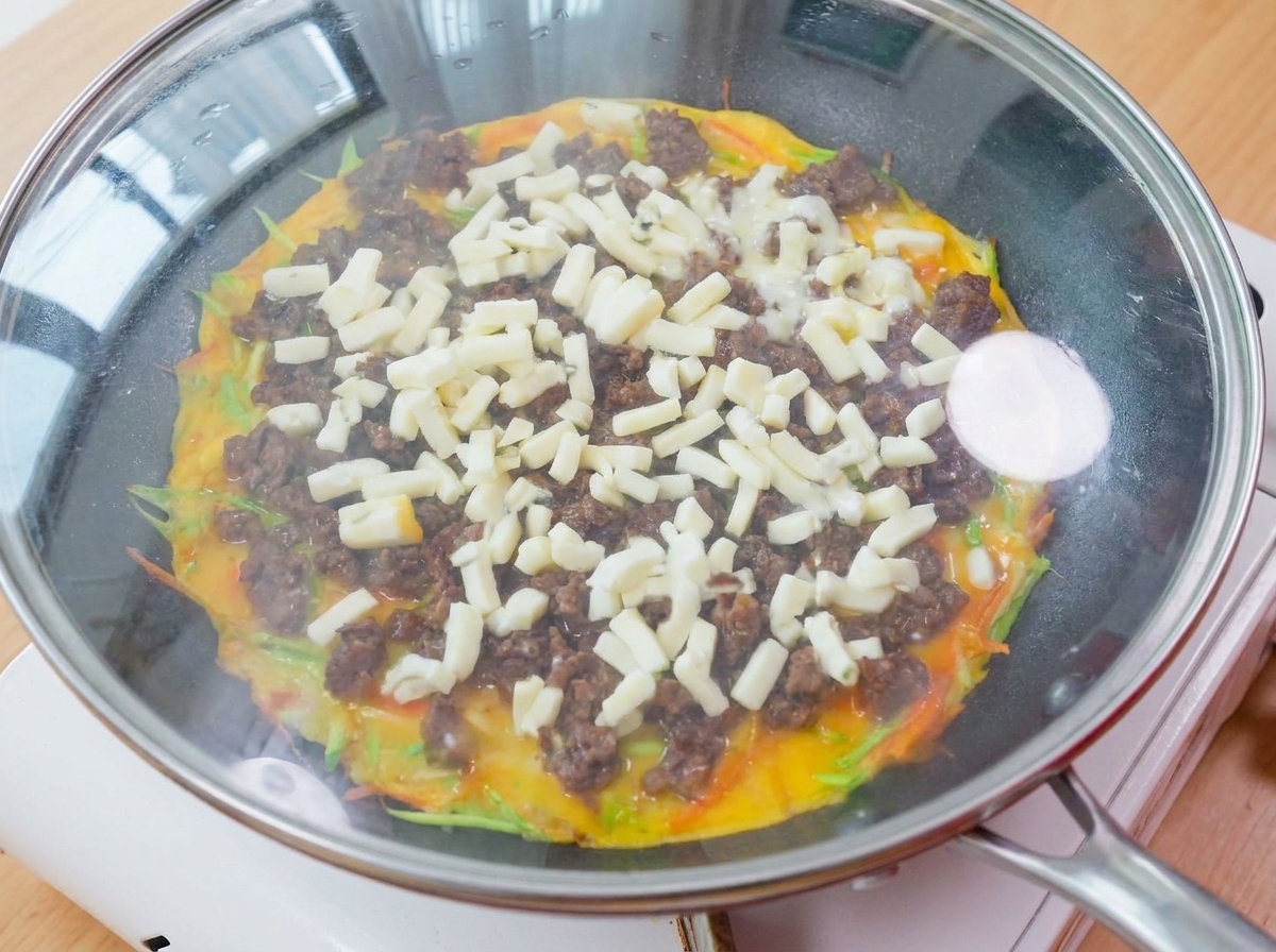 Une poêle recouverte dun couvercle en verre reposant sur une cuisinière, avec de la vapeur et du fromage fondait visible à lintérieur.