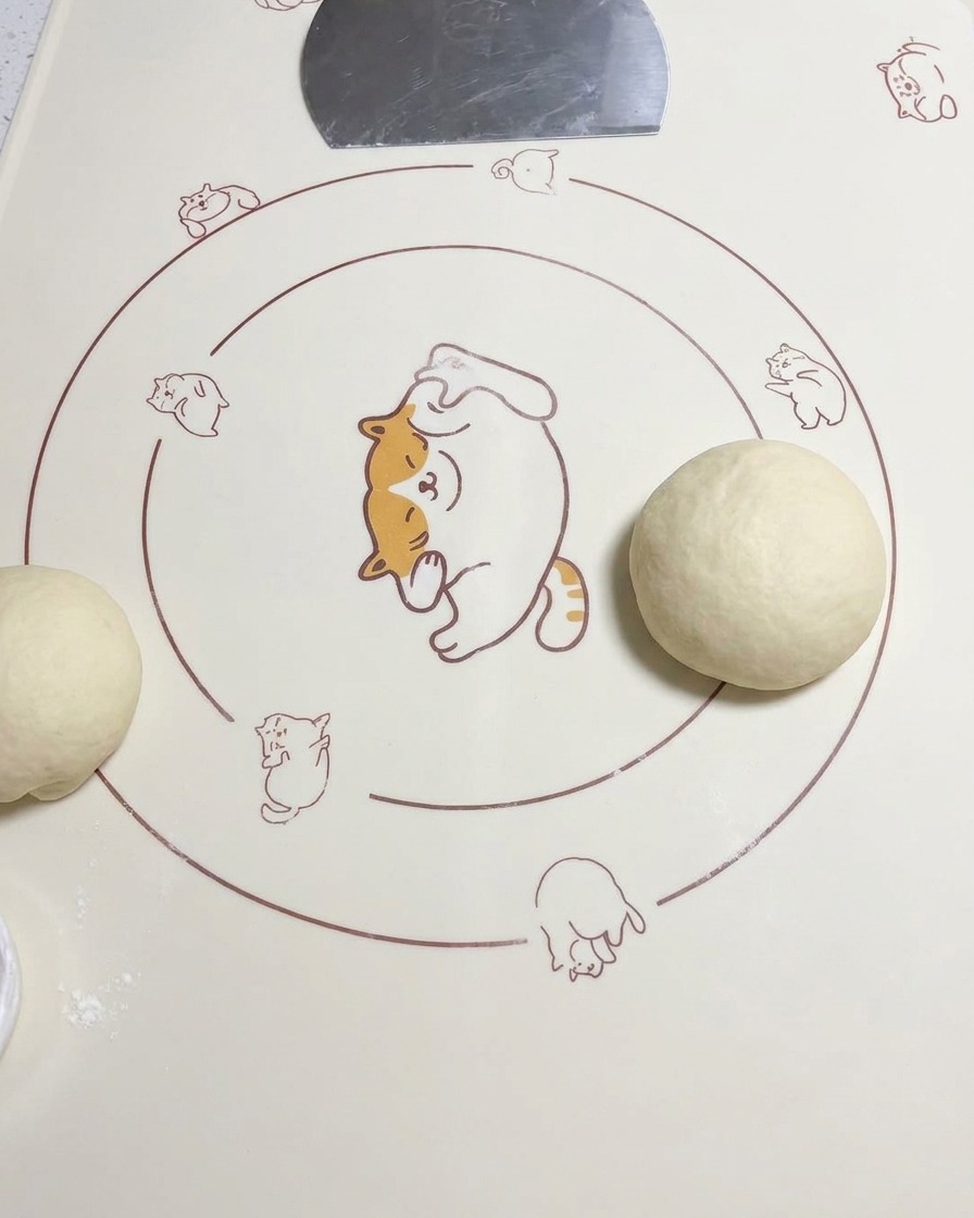 Une boule de pâte arrondie posée sur un tapis en silicone à côté dun autre morceau de pâte abaissée.