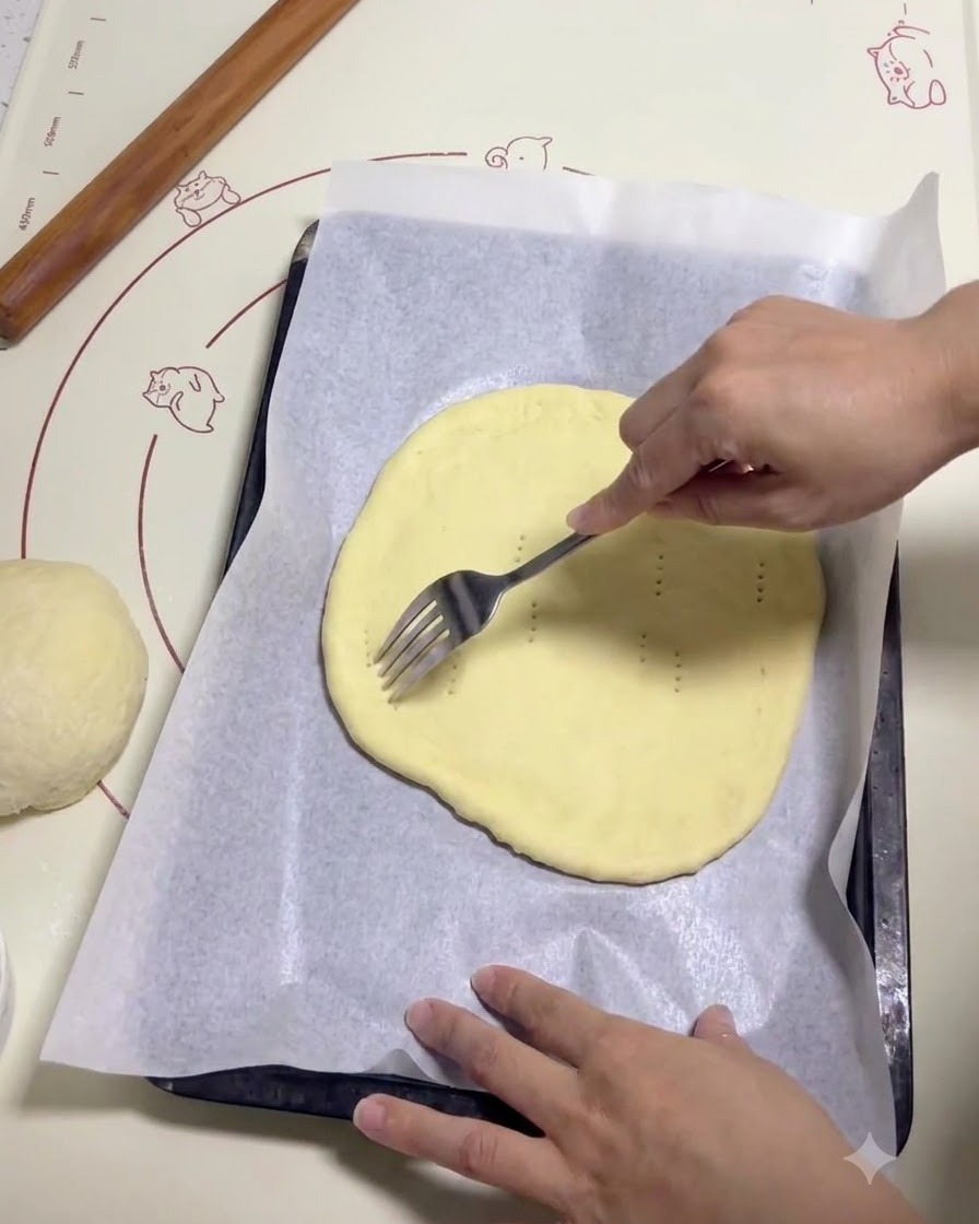 Une main utilisant une fourchette en métal pour percer de petits trous sur un morceau de pâte à pizza plat et rond sur du papier sulfurisé.