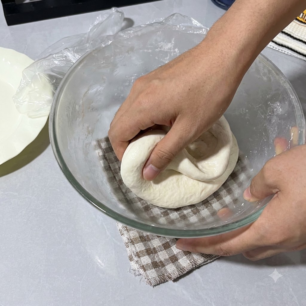 Mains vaporisées deau pliant la pâte dans le bol en verre recouvert dun film plastique.