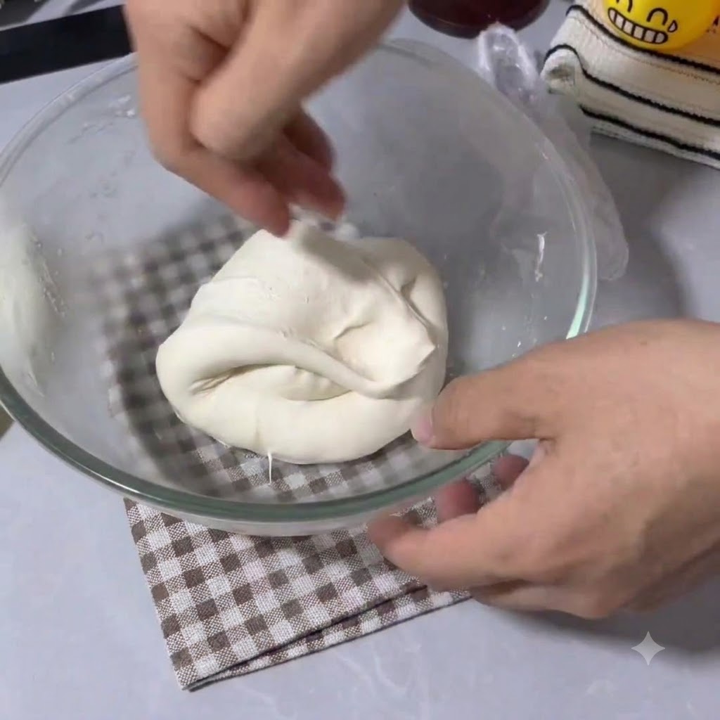 Mains pliant et étirant la pâte à pizza élastique dans un bol à mélanger en verre transparent.