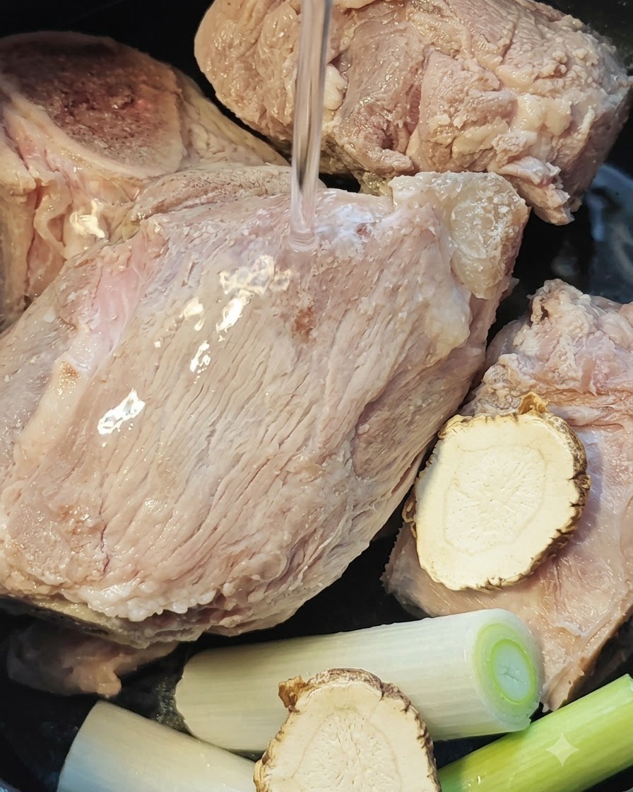 De leau versée sur les os de porc, la racine dangélique et les ciboules dans le cuiseur de riz.