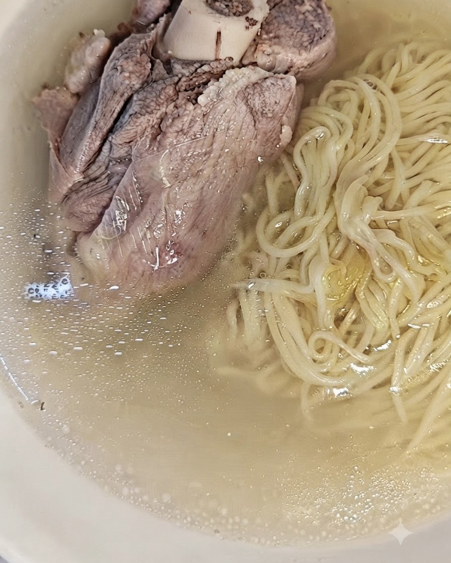 Des nouilles cuites disposées dans un bol à côté du bouillon de porc clair et filtré.