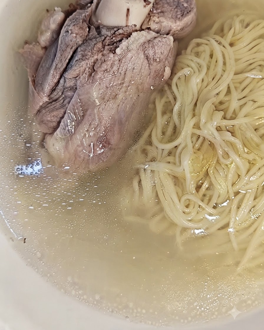 Un grand os de porc cuit placé sur le dessus des nouilles et du bouillon dans un bol, prêt à être servi.