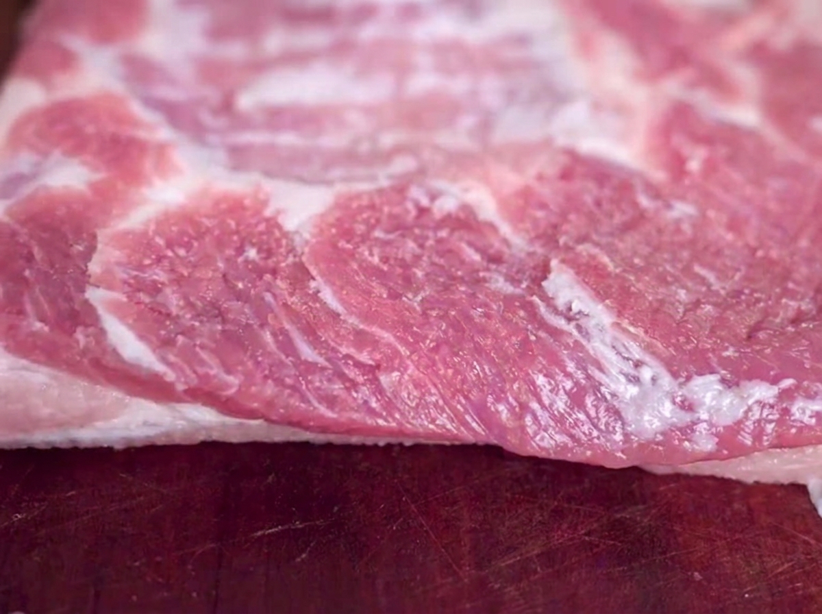 Gros plan dune tranche de poitrine de porc crue posee sur une planche a decouper en bois avec des grains de sel visibles.