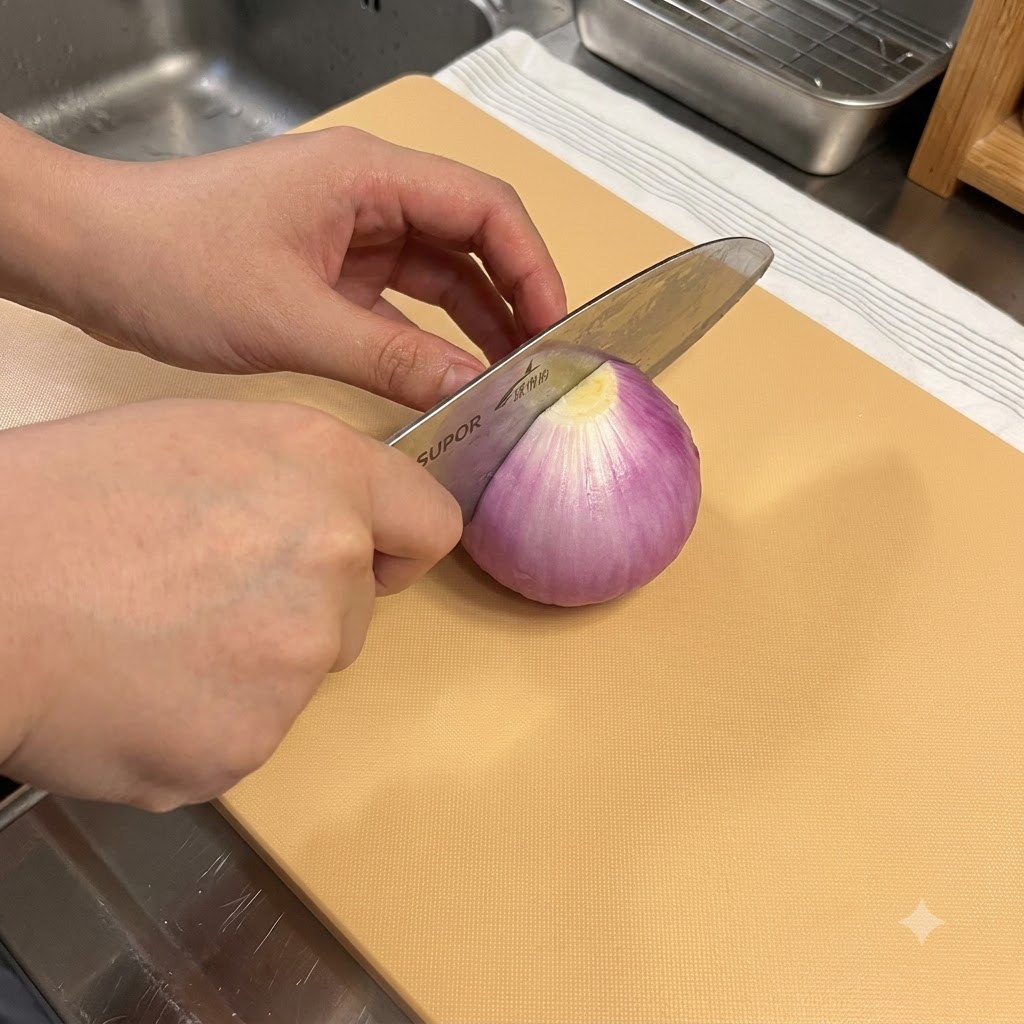 Un couteau de cuisine coupant un oignon rouge sur une planche à découper en bois.