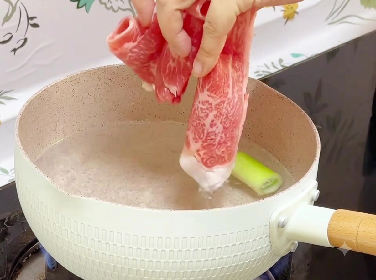 Des rouleaux de bœuf surgelés jetés dans une casserole deau bouillante avec un morceau de ciboule à lintérieur.