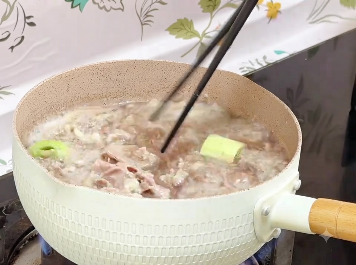Des baguettes récupérant des rouleaux de bœuf blanchis dune casserole bouillante vers un récipient.