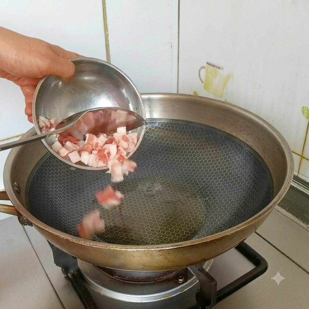 Des dés de poitrine de porc versés dun petit bol dans un wok en acier inoxydable chaud et huilé.