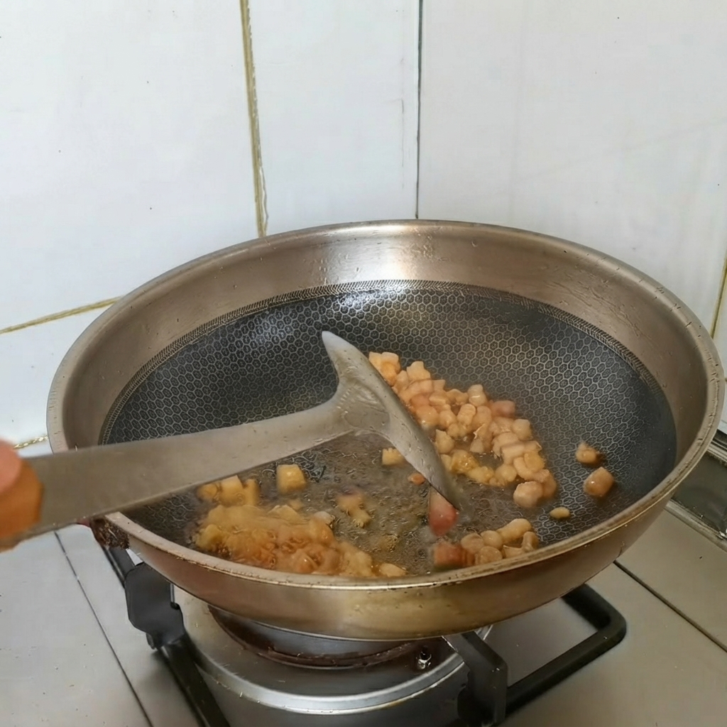 Morceaux de poitrine de porc dorés en train dêtre sautés dans un wok avec des aromates.