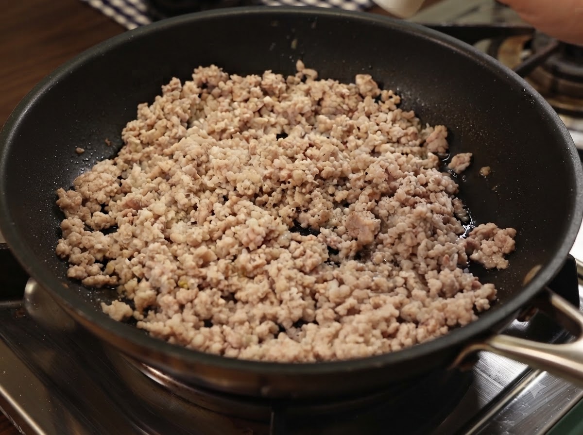 Du poivre noir moulu et du sel de mer saupoudrés sur le porc haché cuit dans une poêle.