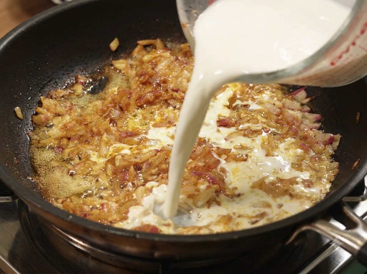 Du lait versé dune tasse à mesurer dans une poêle doignons et de curry frémissants.