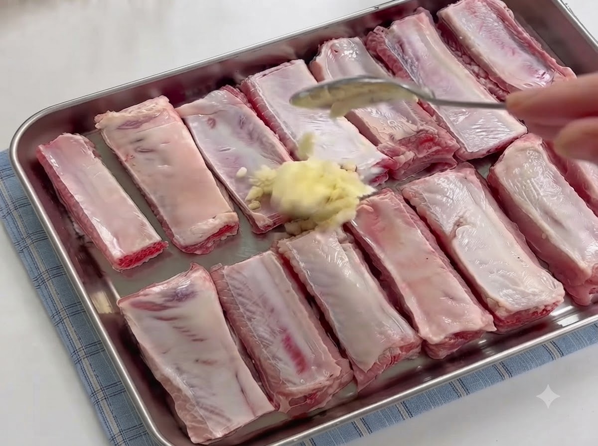 Une cuillère ajoutant un dôme dail fraîchement émincé sur les travers de porc crus dans un platcite: 1.