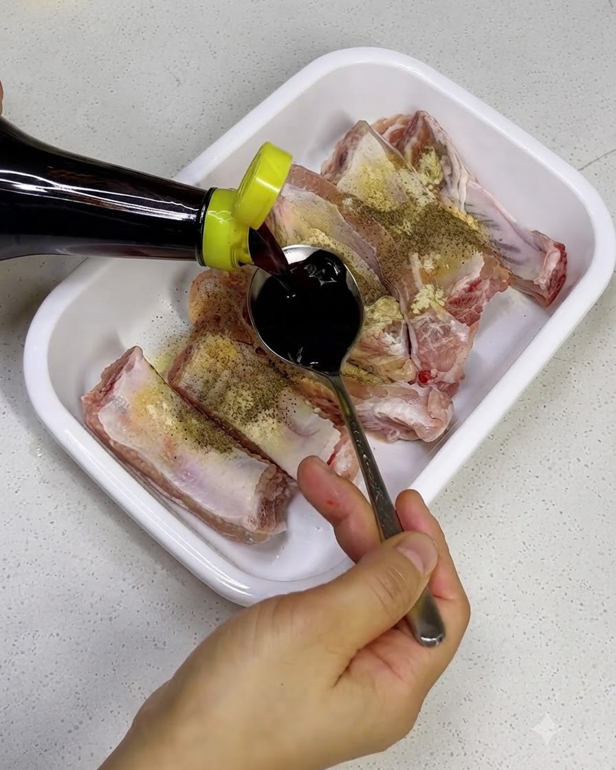 Verser de la sauce soja noire dune bouteille sur des travers de porc crus dans un plateau blanc.