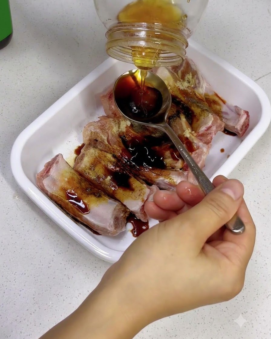 Main tenant une cuillère pour attraper du miel doré versé dun pot en verre sur des travers de porc assaisonnés.