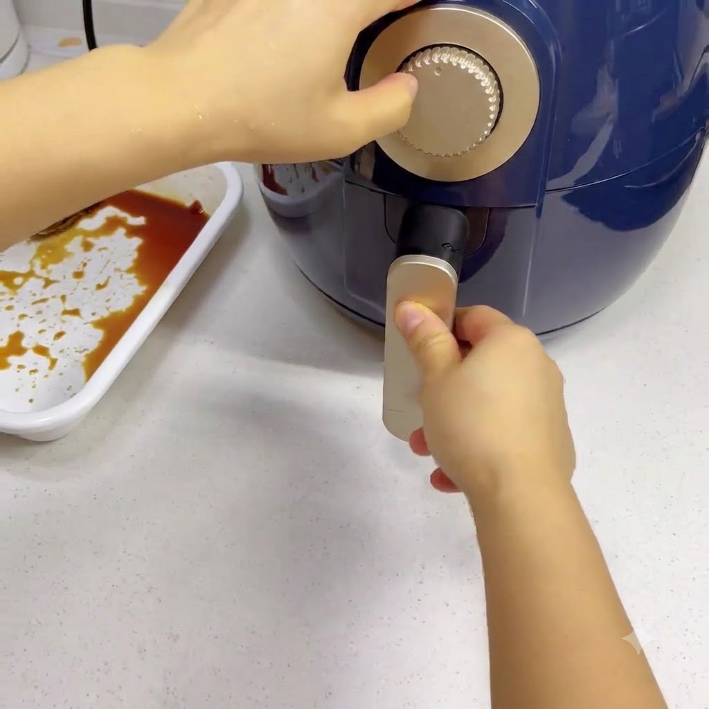 Une main tournant le minuteur argenté dun air fryer bleu foncé.