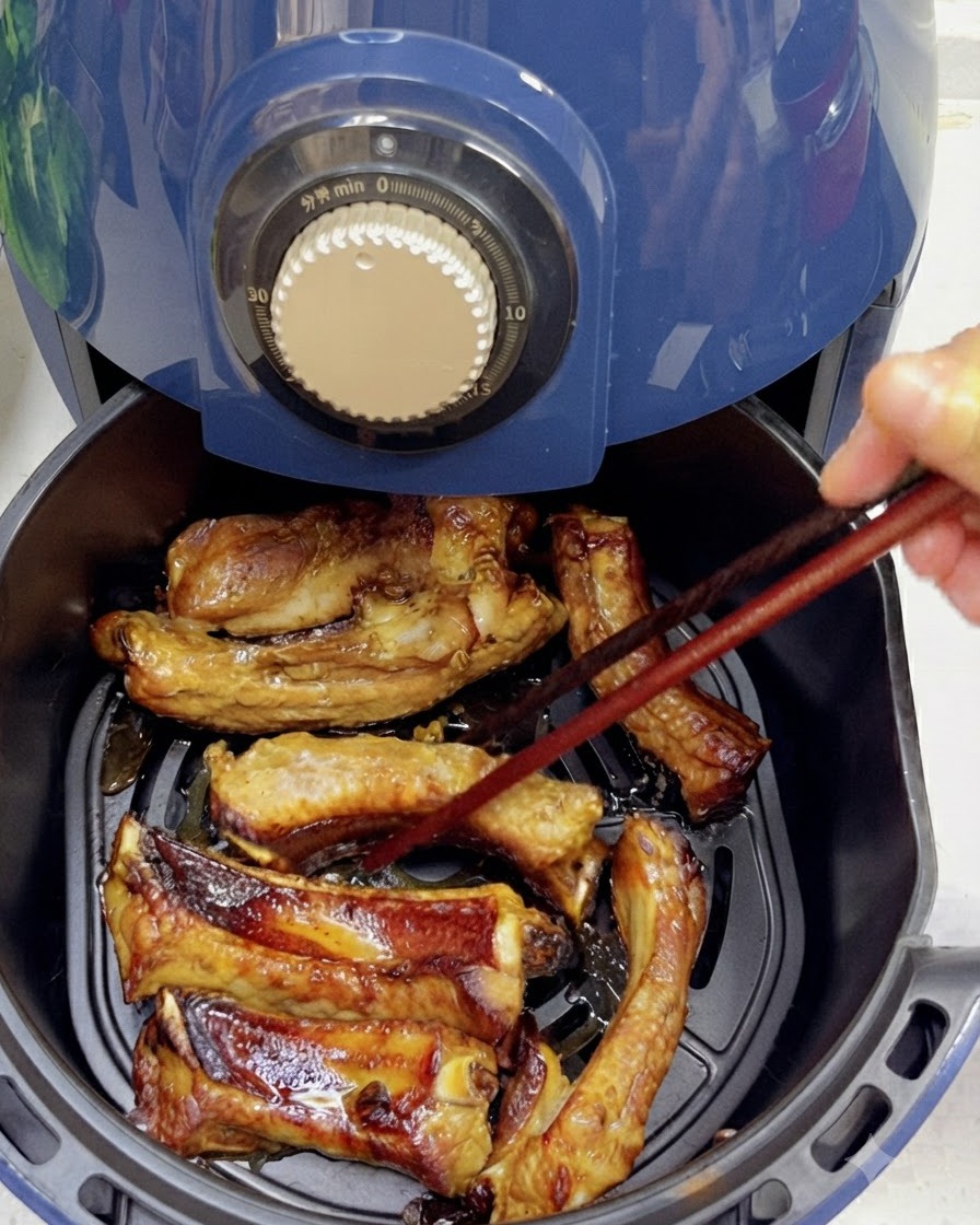 Utilisation de baguettes pour retourner des travers de porc partiellement cuits et dorés à lintérieur dun panier de air fryer.