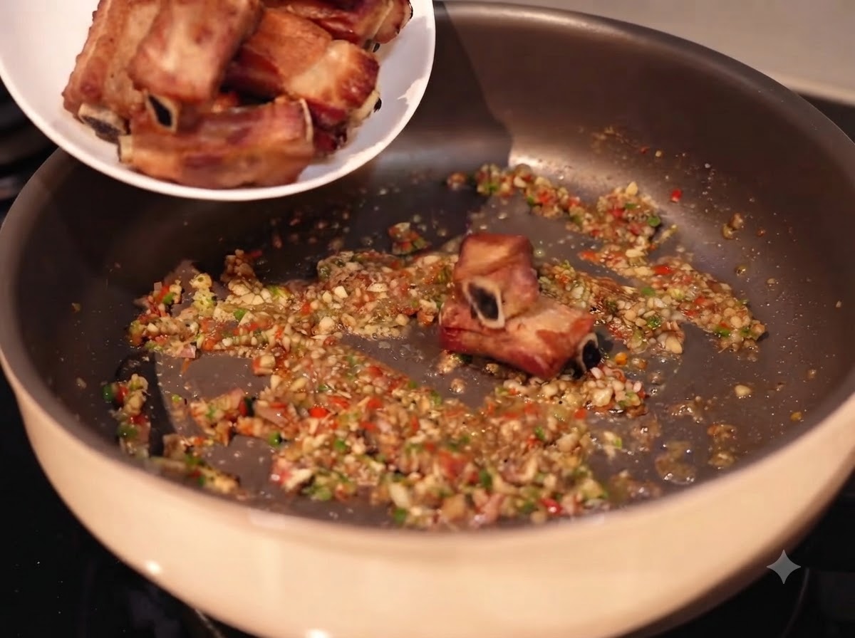 Côtes de porc ajoutées dune assiette blanche dans une poêle remplie dail émincé sauté, de piments et dépices.