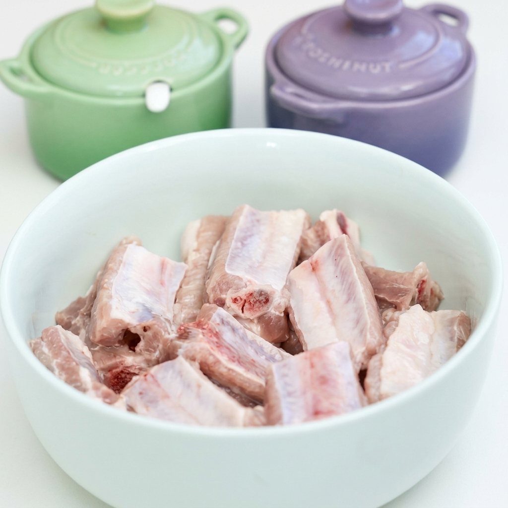 Côtes de porc crues dans un bol blanc assaisonnées avec de lail, des sauces soja, de la sauce huître et des épices.