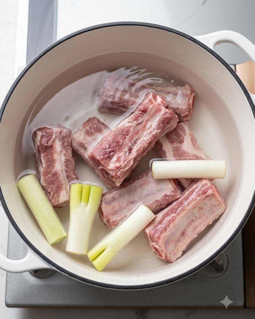Travers de porc frais dans une marmite deau froide avec des oignons verts et des aromates avant ébullition.