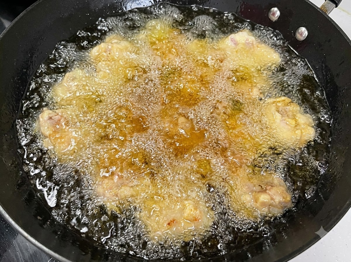 Plusieurs morceaux de côtes de porc en train de frire dans de lhuile chaude et bouillonnante à lintérieur dun wok noir.