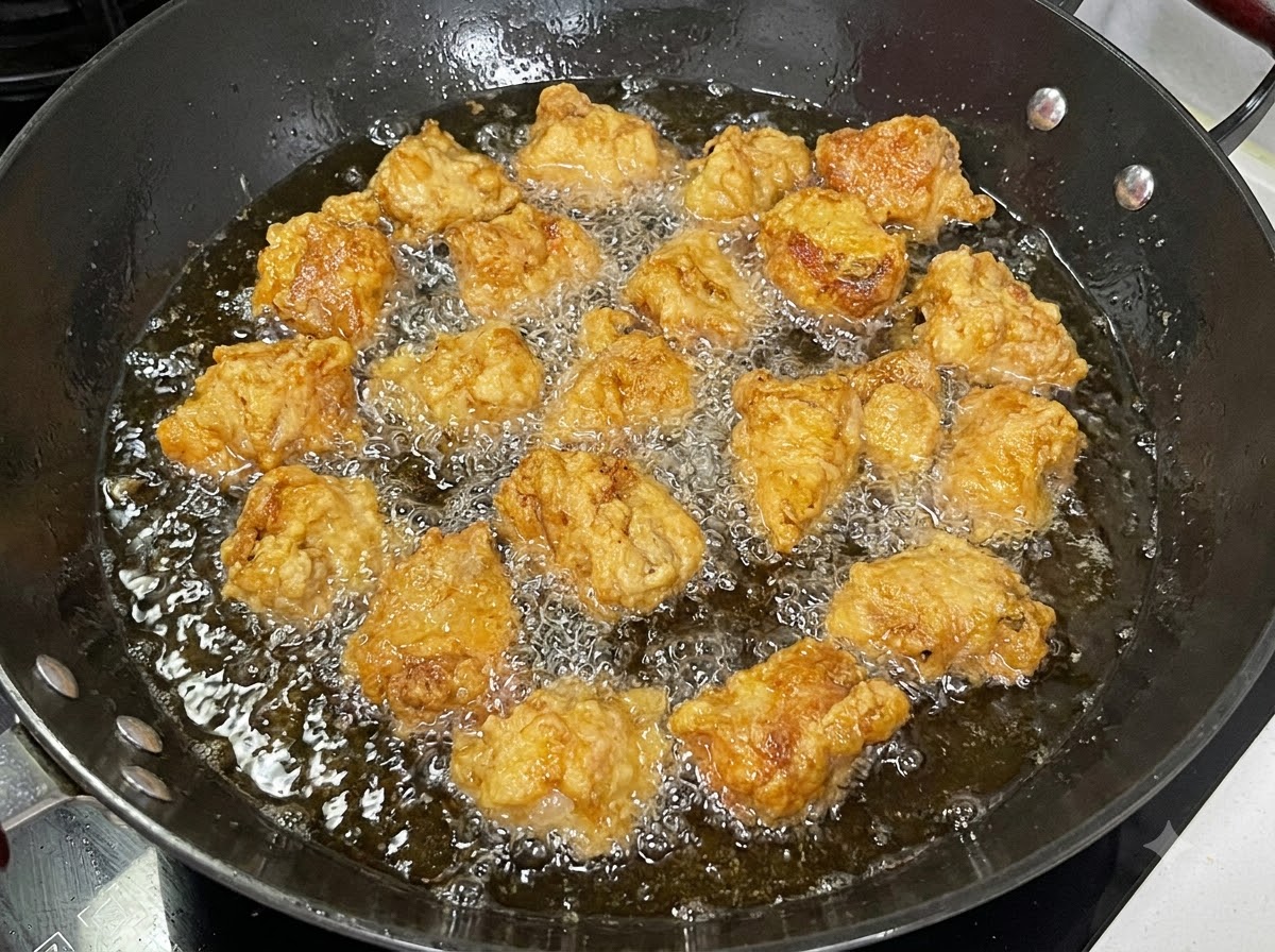 Morceaux de côtes de porc enrobées en train de frire dans un wok noir rempli dhuile bouillonnante.