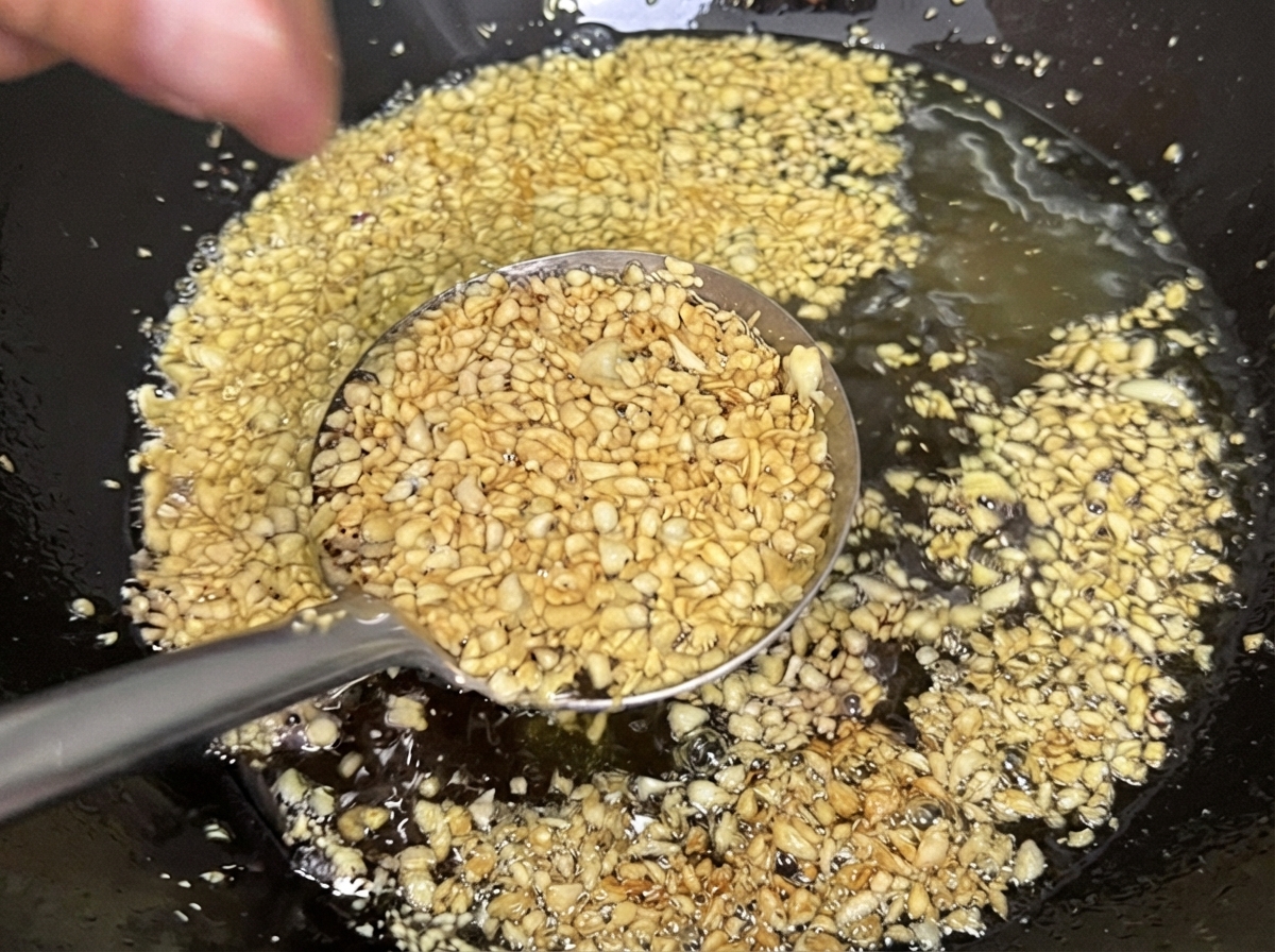 De lail émincé en train de frire dans lhuile à lintérieur dun wok, prenant une teinte jaune doré claire et croustillante.