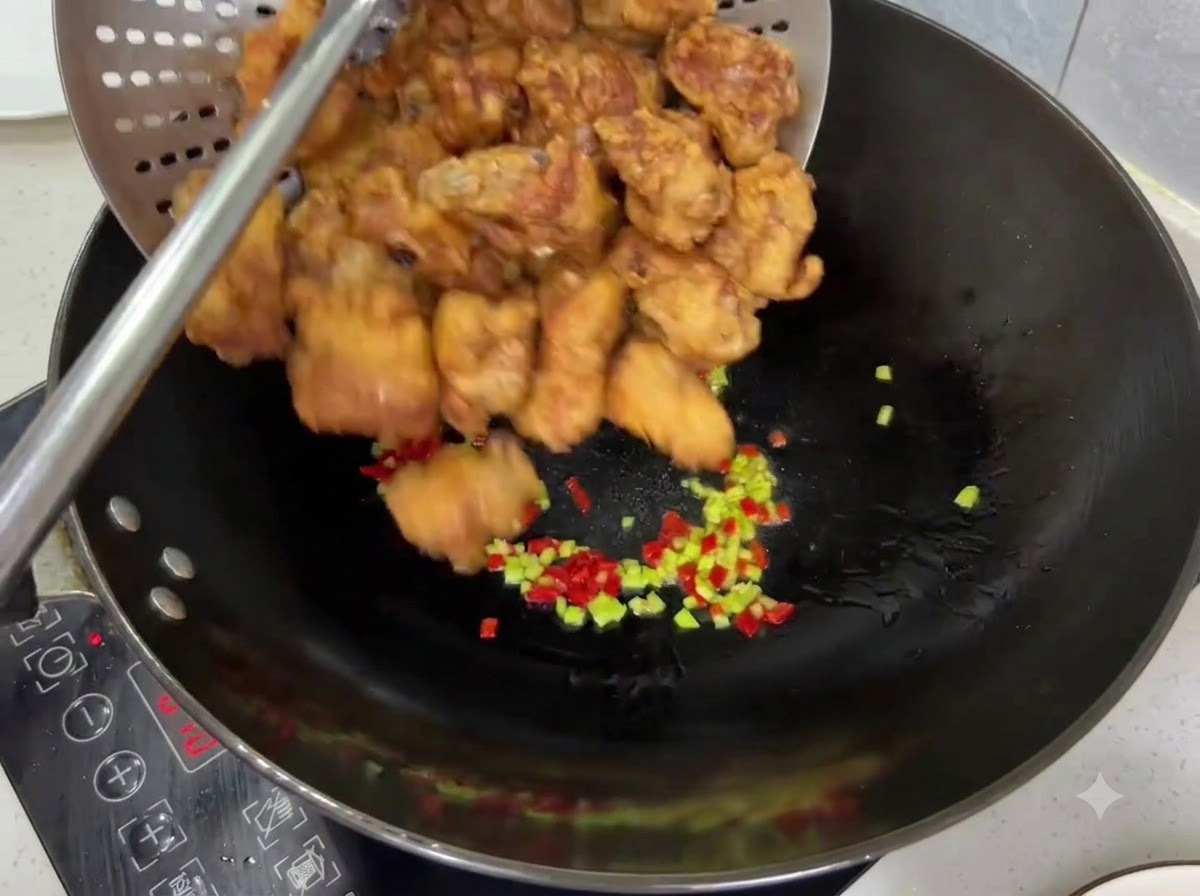Côtes de porc frites dorées et croustillantes versées dune passoire dans un wok avec des piments.