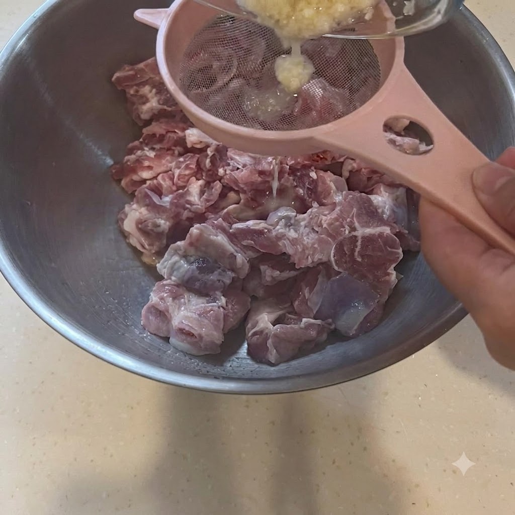 Purée dail filtrée à travers un tamis rose directement au-dessus dun grand bol de morceaux de porc crus.
