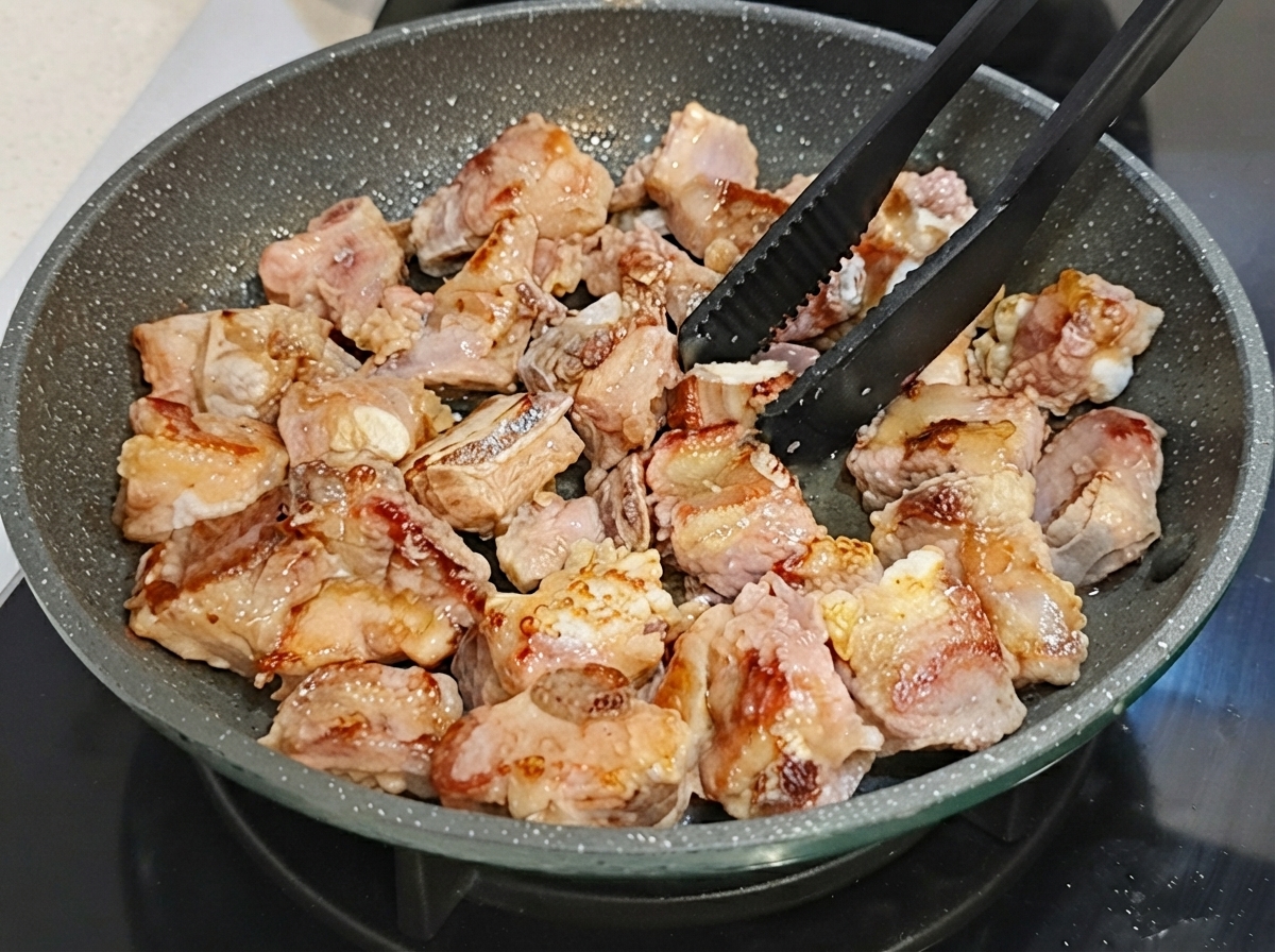 Côtes de porc retournées dans une poêle à frire antiadhésive à laide de pinces noires.