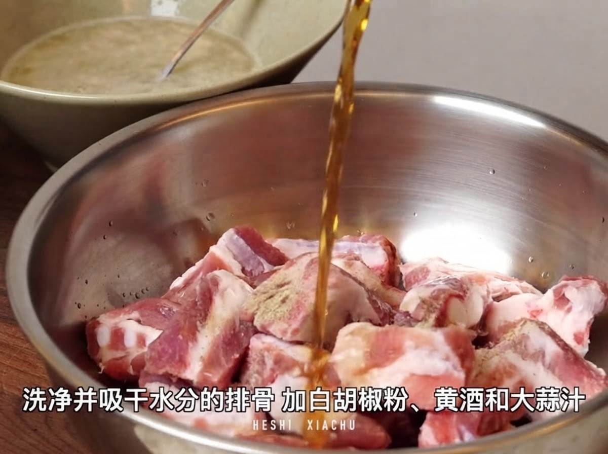 Vin jaune versé par le haut dans un bol mélangeur en métal rempli de morceaux de côtes de porc coupés saupoudrés de poudre de poivre blanc.